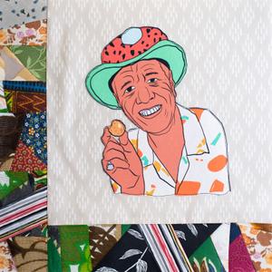 Wally Amos smling in a bright colored hat and holding a cookie in his hand.